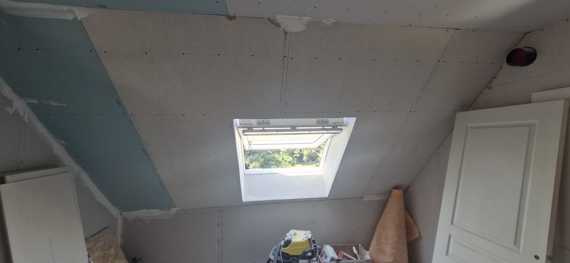 Aménagement de combles : pose de placo au plafond autour d'une fenêtre de toit Velux