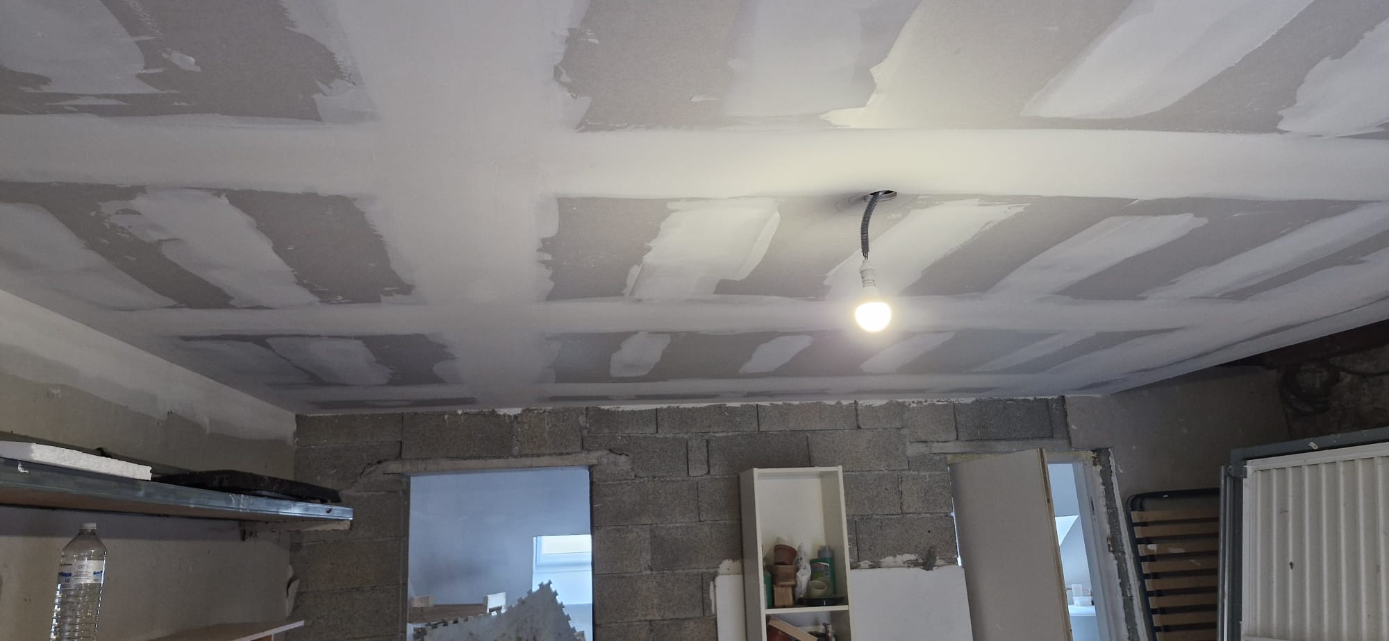 Enduits et bandes sur plafond placo dans une pièce en rénovation avec murs en parpaings