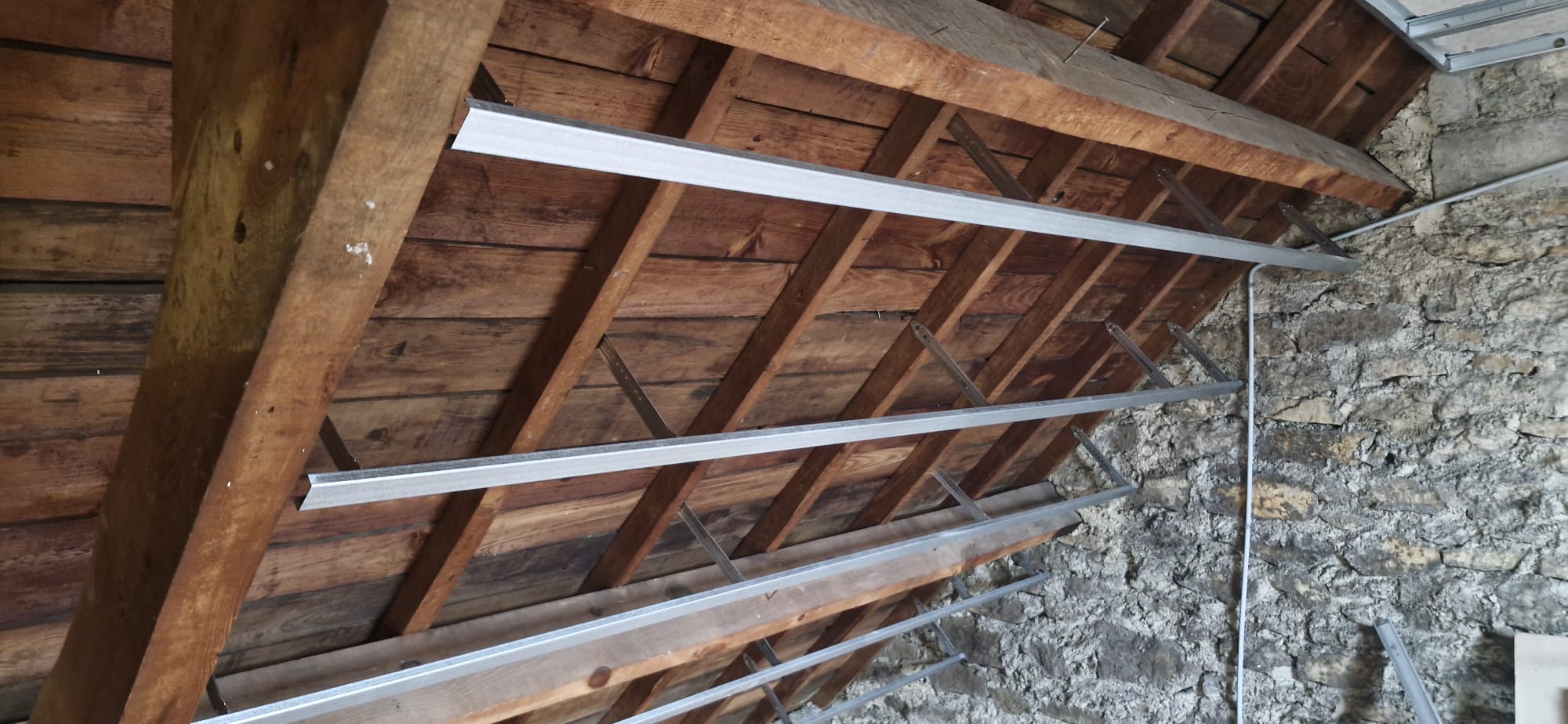 Rails métalliques posés sous charpente bois ancienne avant isolation et placo — grange rénovée